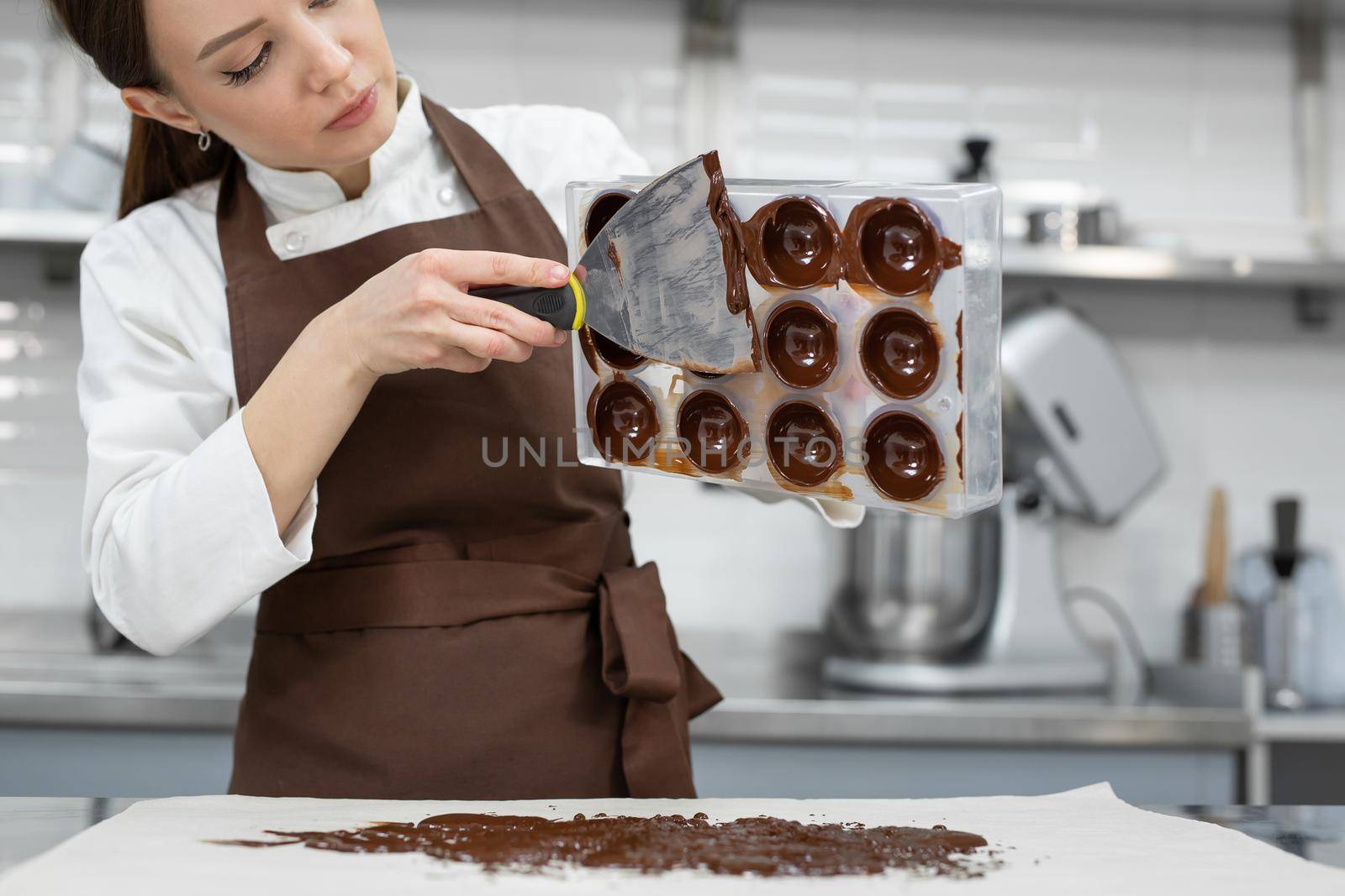 Chef or chocolatier makes sweet chocolates in a professional kitchen. She turns the mold over and pours the rest of the chocolate onto the table.