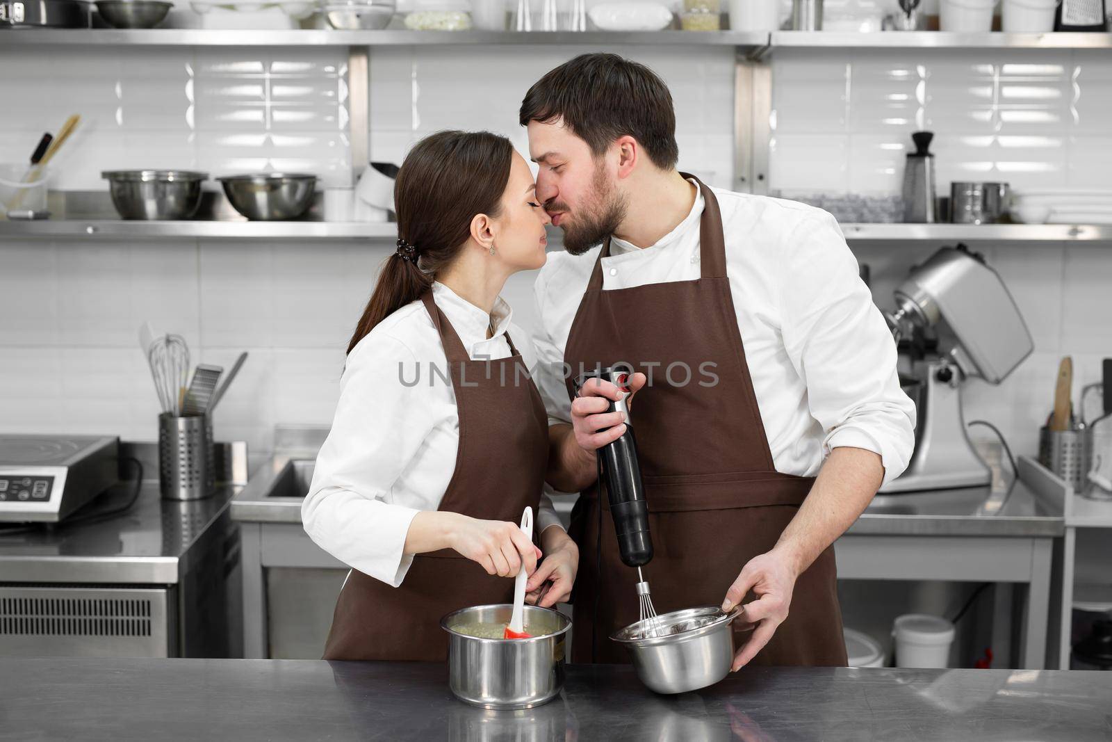 Couple of loving confectioners, a man and a woman, prepare a dessert together in the kitchen, hug and kiss.