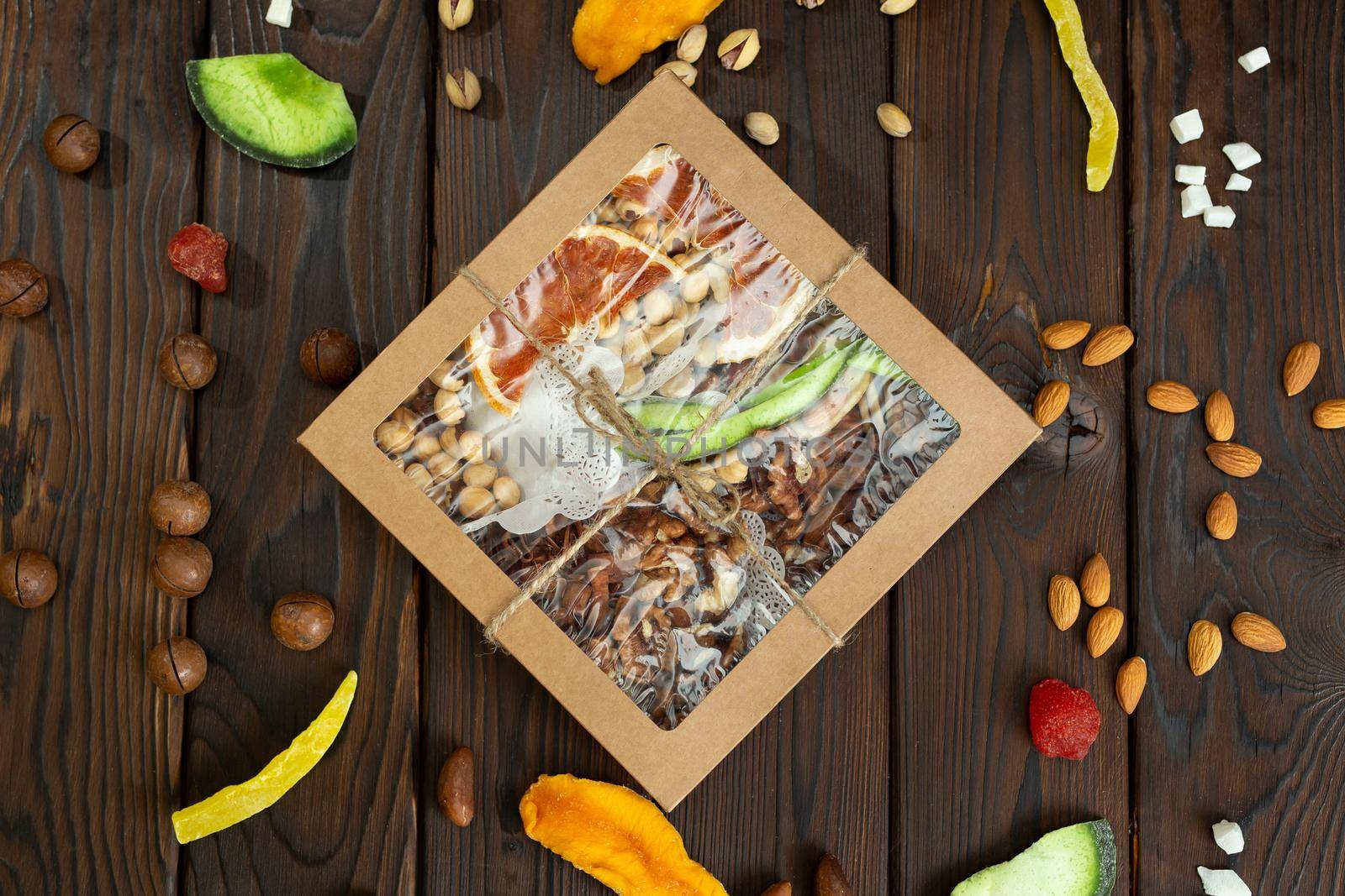 Nuts, candied fruits and dried fruits of different varieties in a paper box on a structural wooden background top view.