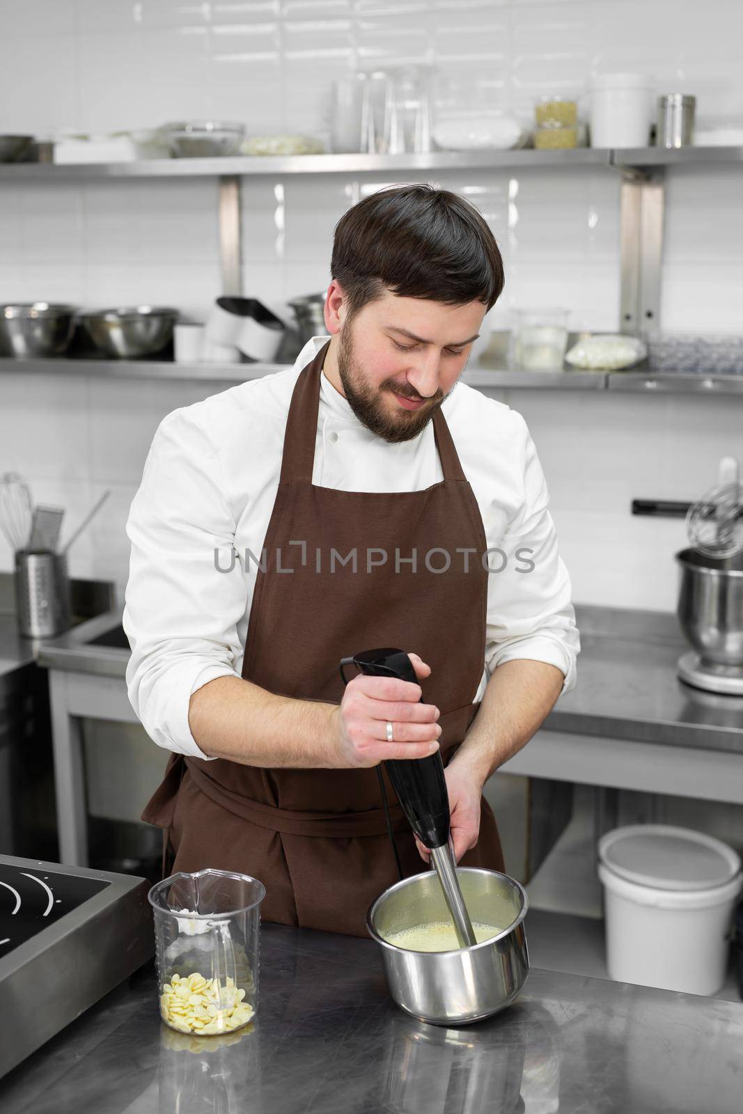 Male pastry chef whips up a mirror icing with white chocolate for a cake using a blender