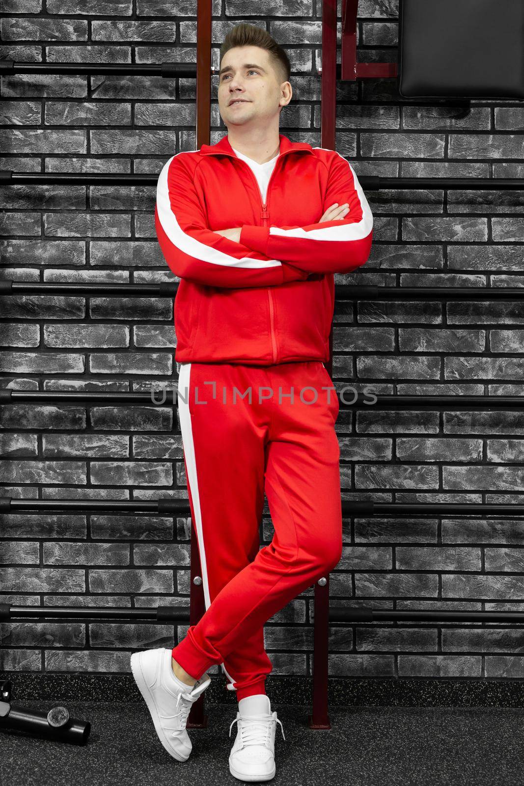 Man in a red tracksuit poses against the wall of the gym.