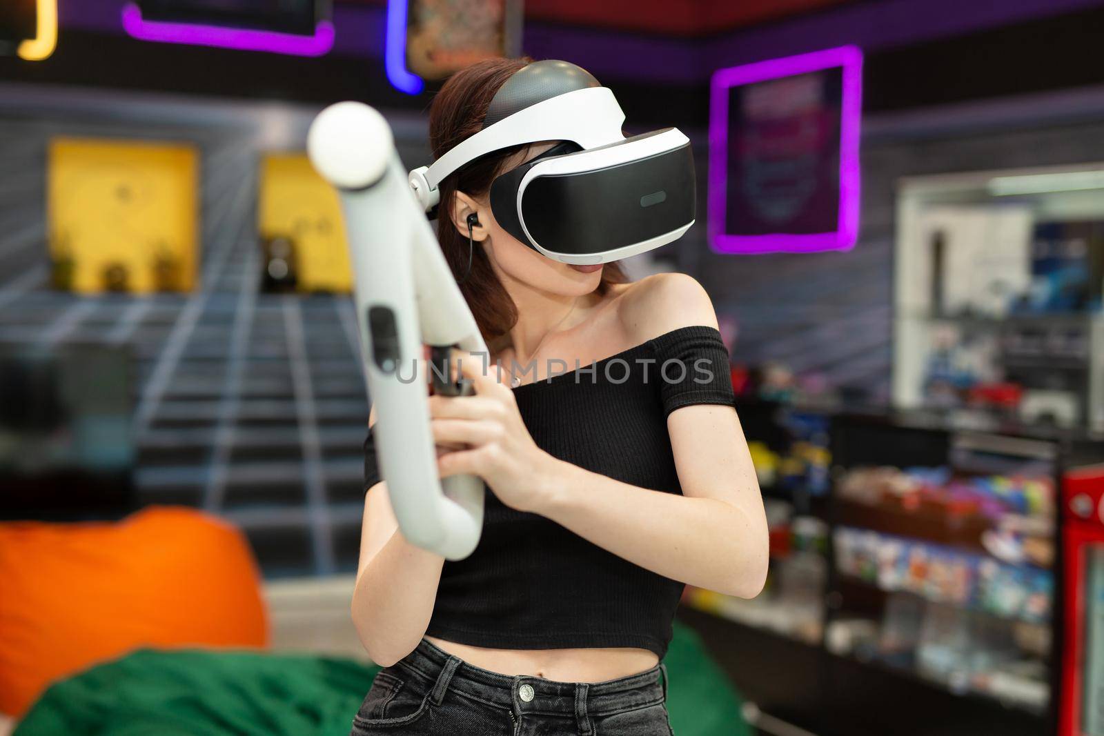 Young woman plays on a video games console, an emotional gamer shoots a game using a gun controller in a game club. VR