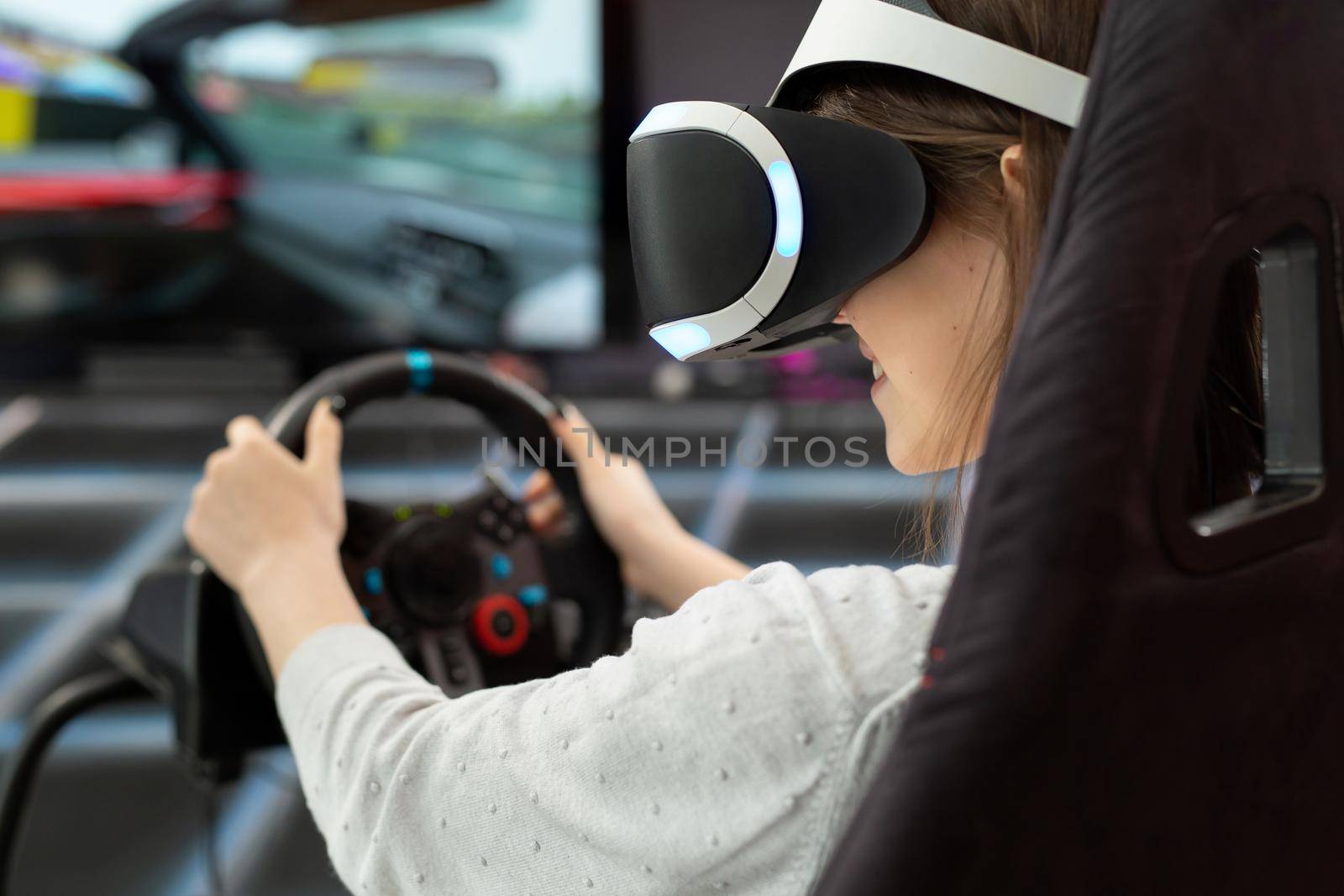 Close-up of the hands of a teenage girl in virtual reality glasses, who is holding the steering wheel and playing a computer game on the console.