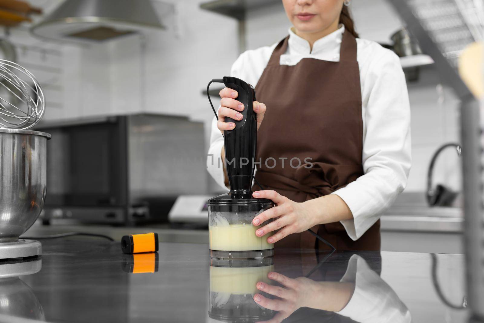 Female pastry chef prepares a mirror icing for a cake, whips it in a blender by StudioPeace