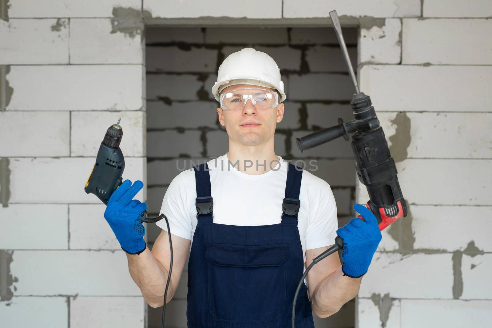 Professional construction worker in a white hard hat is holding a drill and a screwdriver.