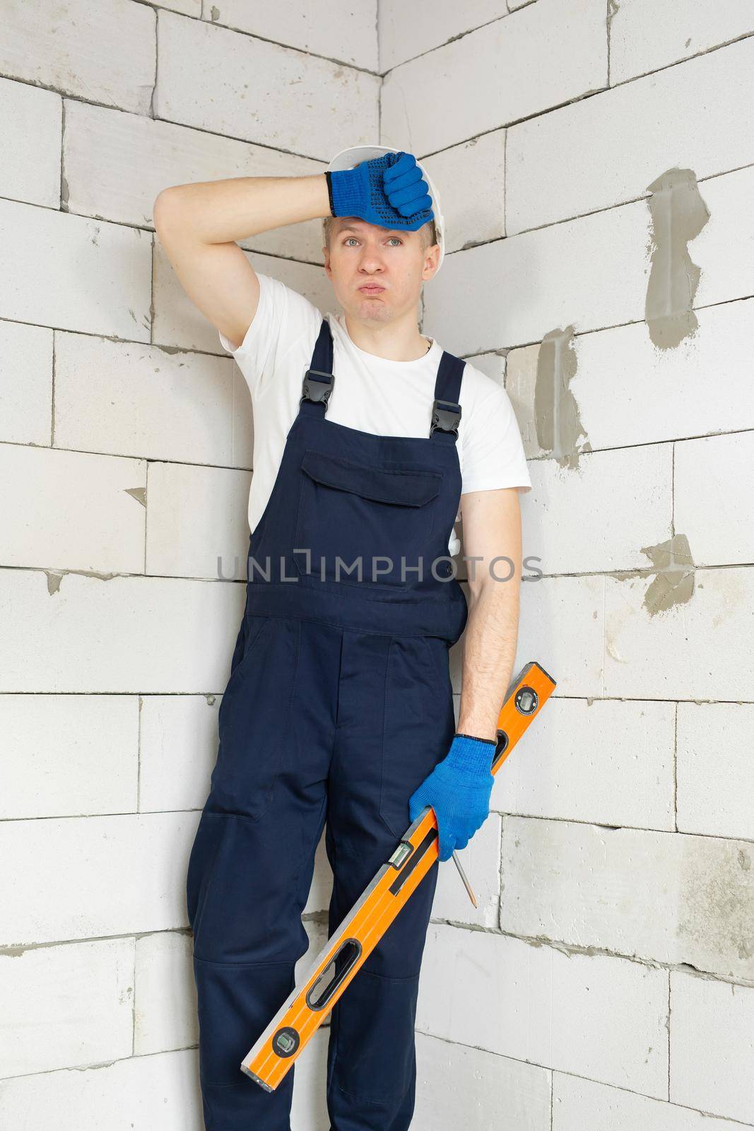 Handsome young architect or builder in a white helmet stands near the wall and rests by StudioPeace