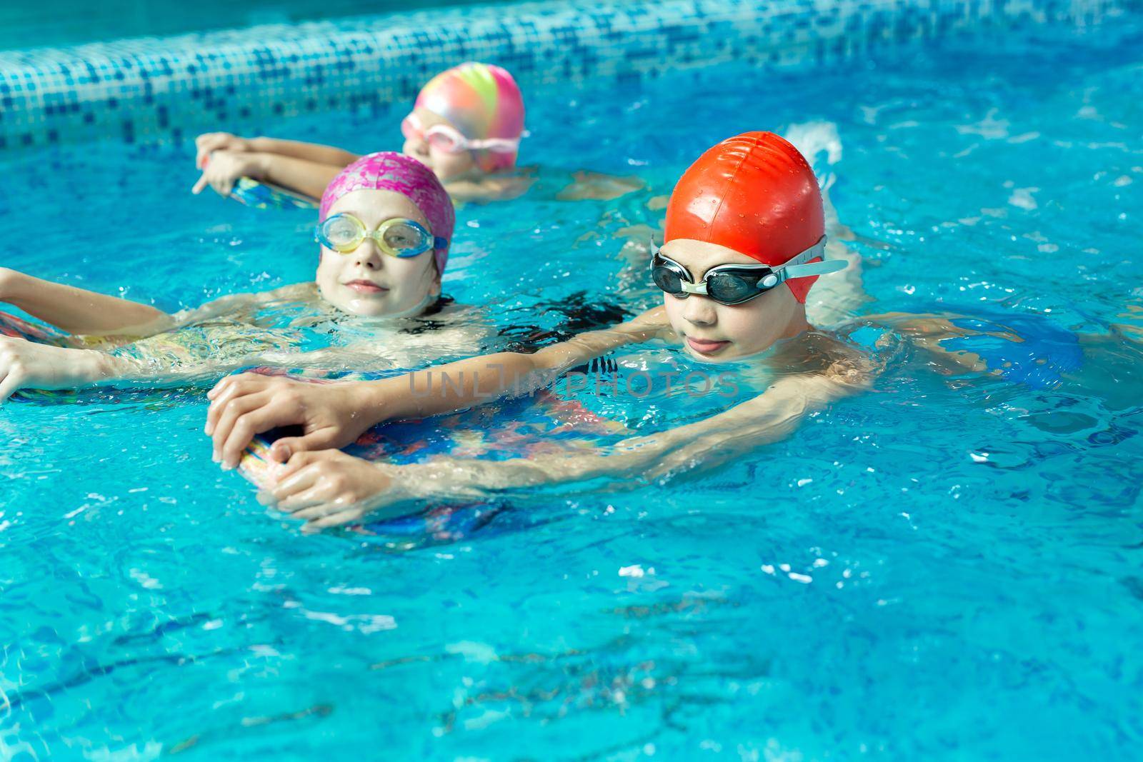 Group of boys and girls train and learn to swim in the pool with an instructor. Development of children's sports.