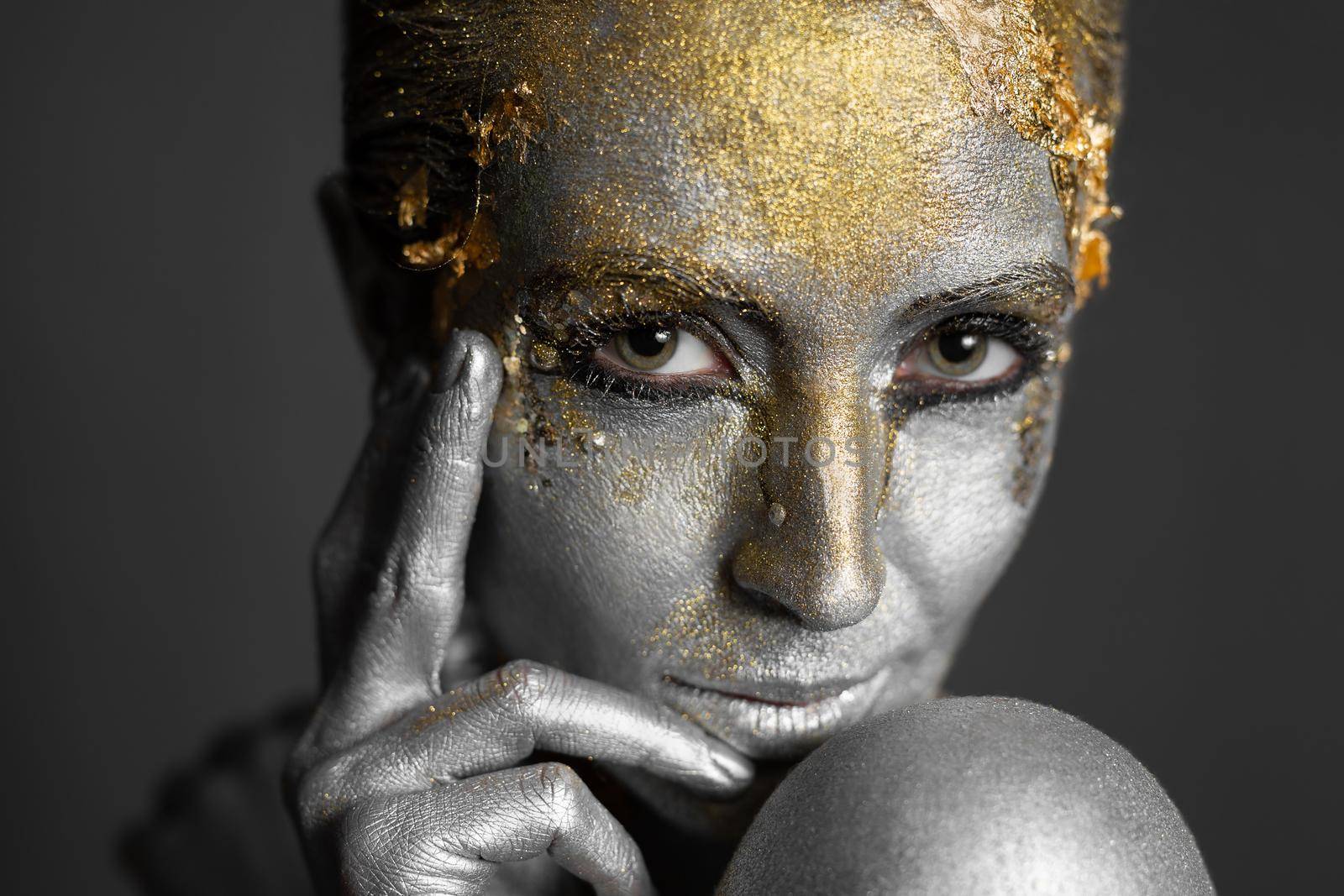 Portrait of a beautiful female model with gold and silver paint on her skin and hair in the studio.