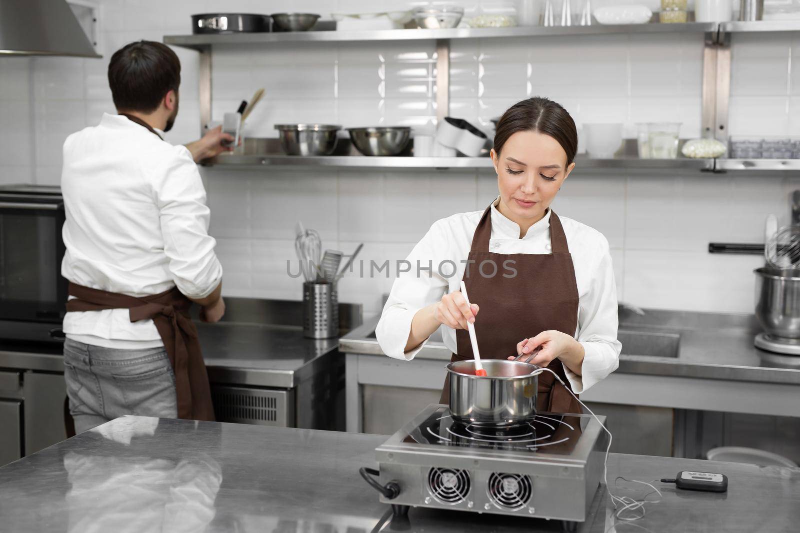 Man and woman confectioners prepare dessert together in a professional kitchen.