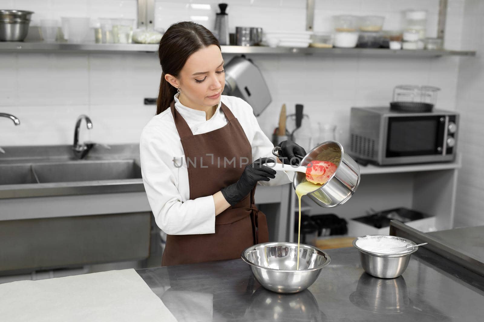 Female pastry chef pours melted white chocolate from a saucepan into a mousse bowl by StudioPeace