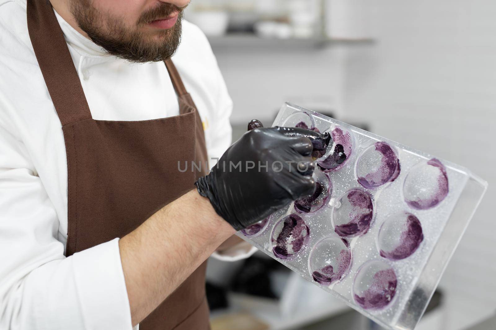 Close-up of the hands of a male pastry chef, who uses a washcloth to apply shiny candurin to a mold for chocolate spheres by StudioPeace