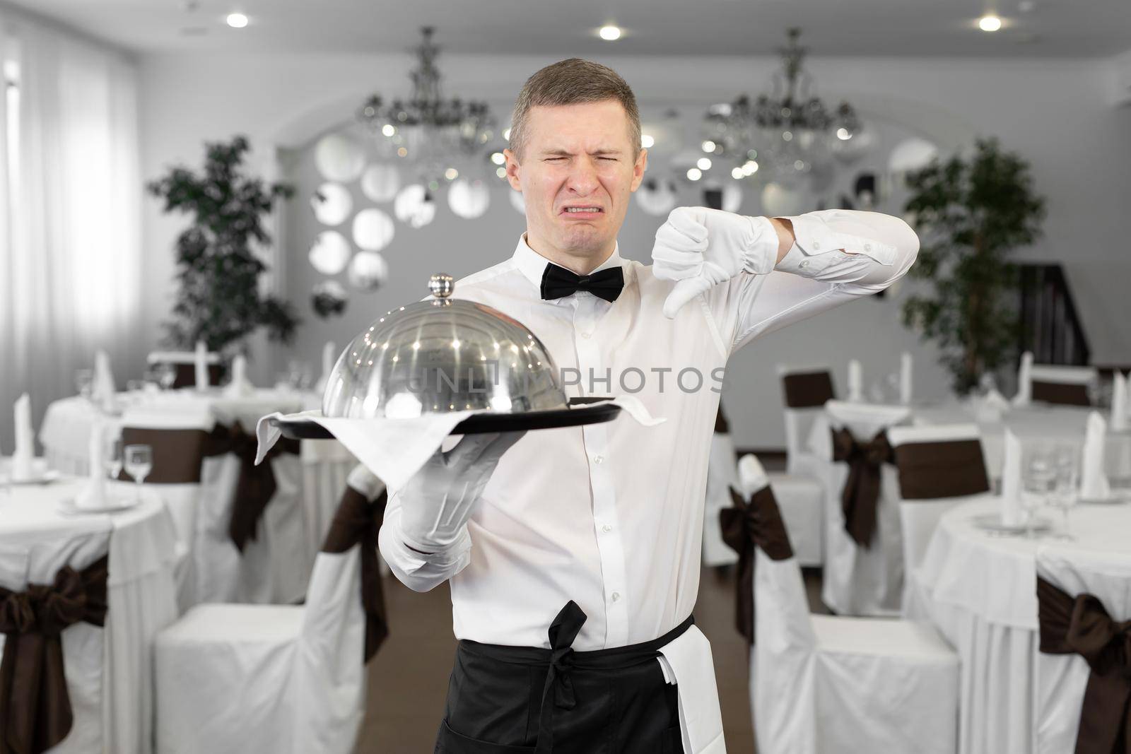 Male waiter in a rstoran with a dish in his hands shows that this dish is tasteless by StudioPeace