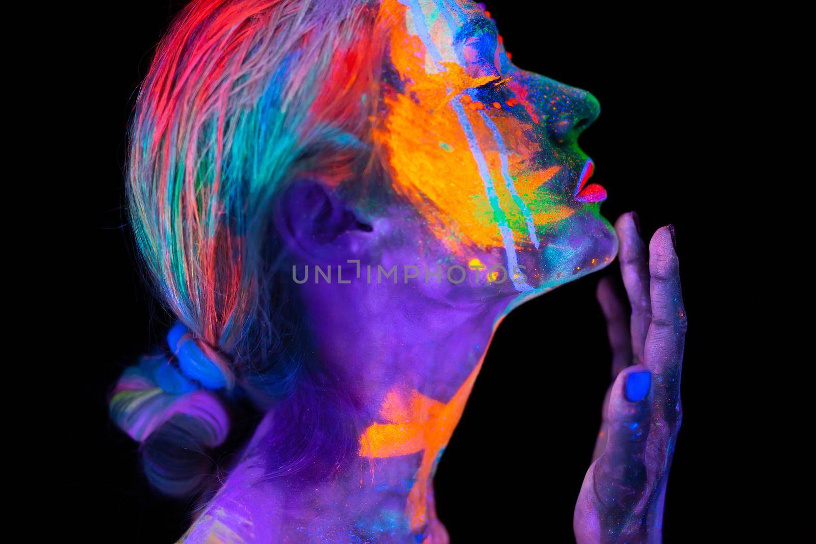 Beautiful young woman in neon light. Portrait of a model with fluorescent makeup posing in UV light with colorful makeup