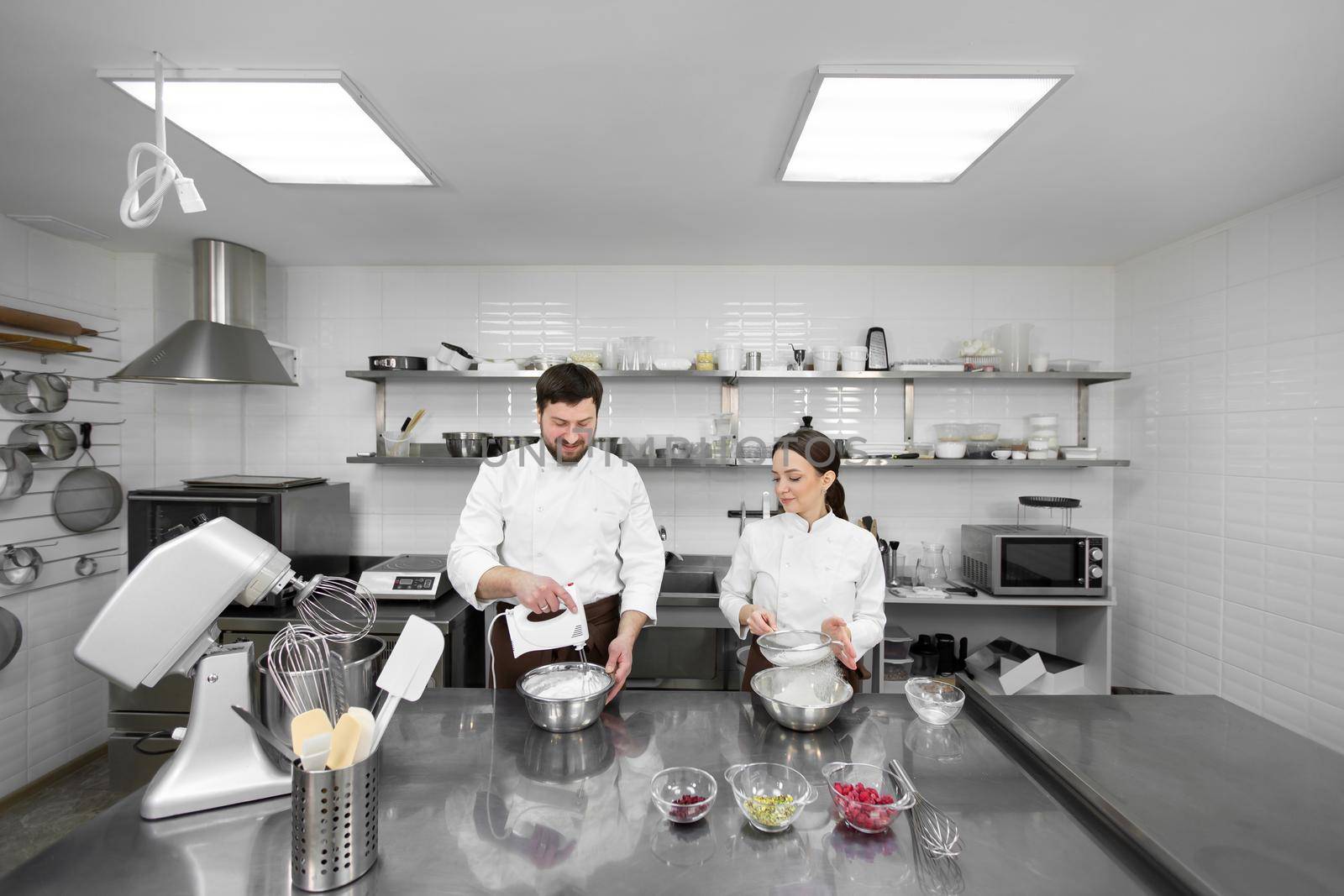 Pastry chef a man and a woman in a professional kitchen prepare a sponge cake, mix the ingredients and sift the flour by StudioPeace