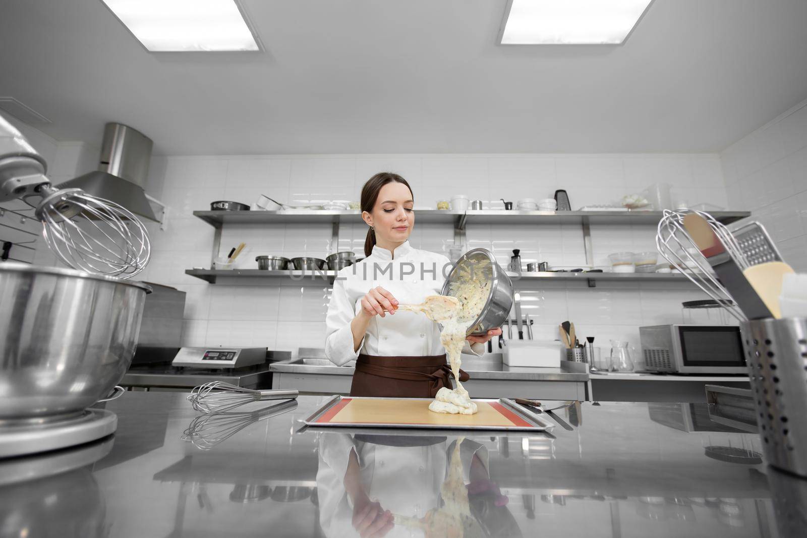 Pastry chef woman pours the dough on a baking sheet with parchment.