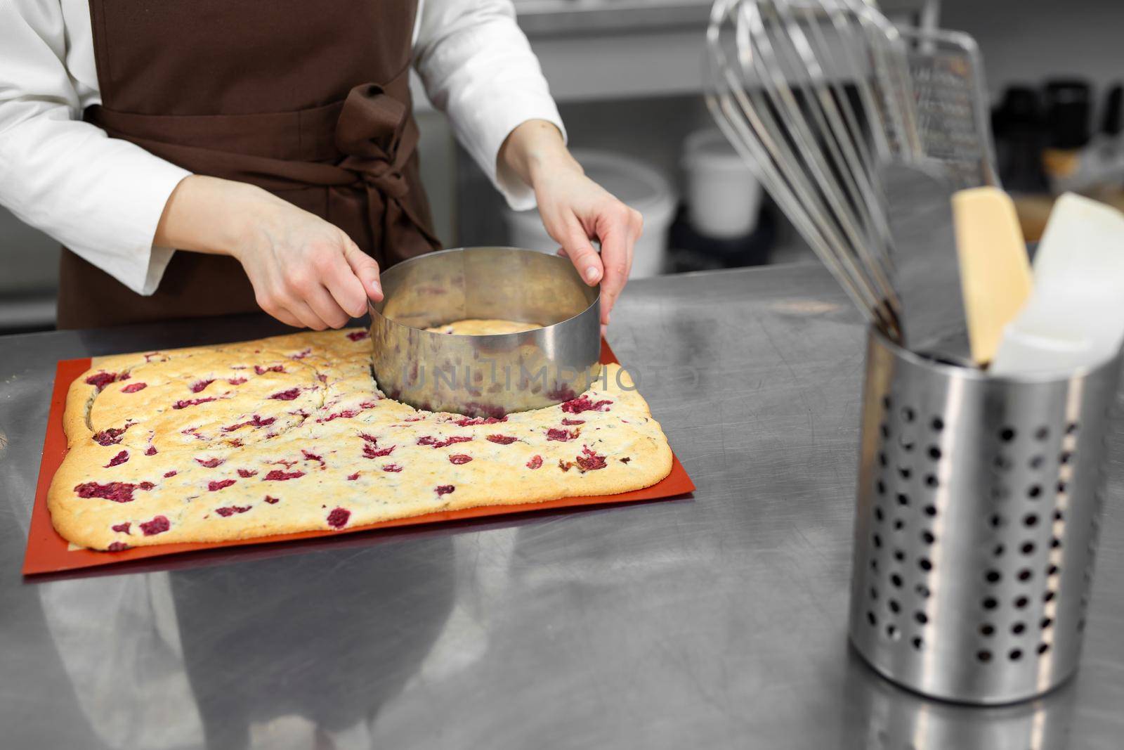 Female pastry chef cuts a round shape out of a large biscuit dough in a professional kitchen by StudioPeace