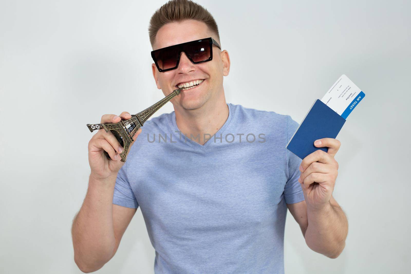 A cheerful young guy in sunglasses with a passport and plane tickets on a white background.