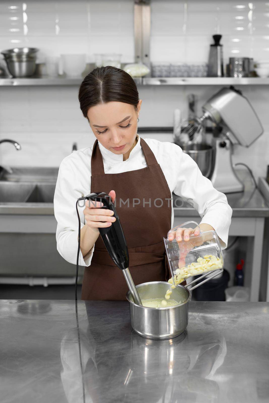 Female pastry chef whips up a mirror icing with white chocolate for a cake with a blender.