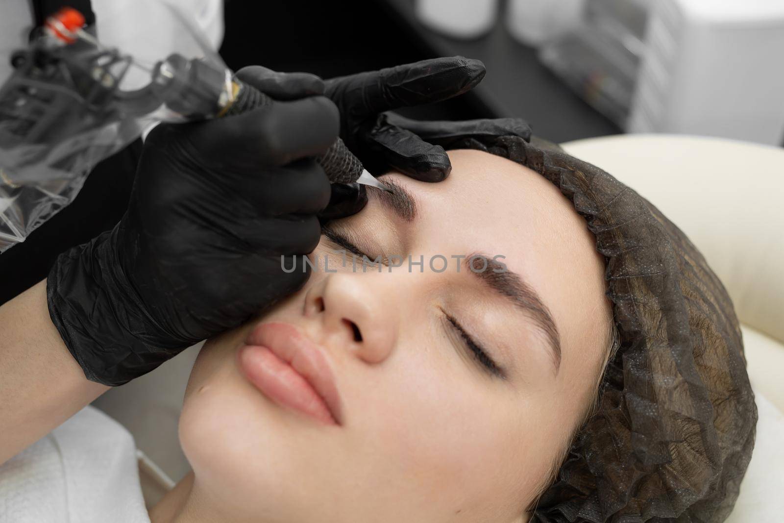 Concept of microblading eyebrows. The cosmetologist performs the procedure of permanent makeup of the eyebrows in close-up by StudioPeace