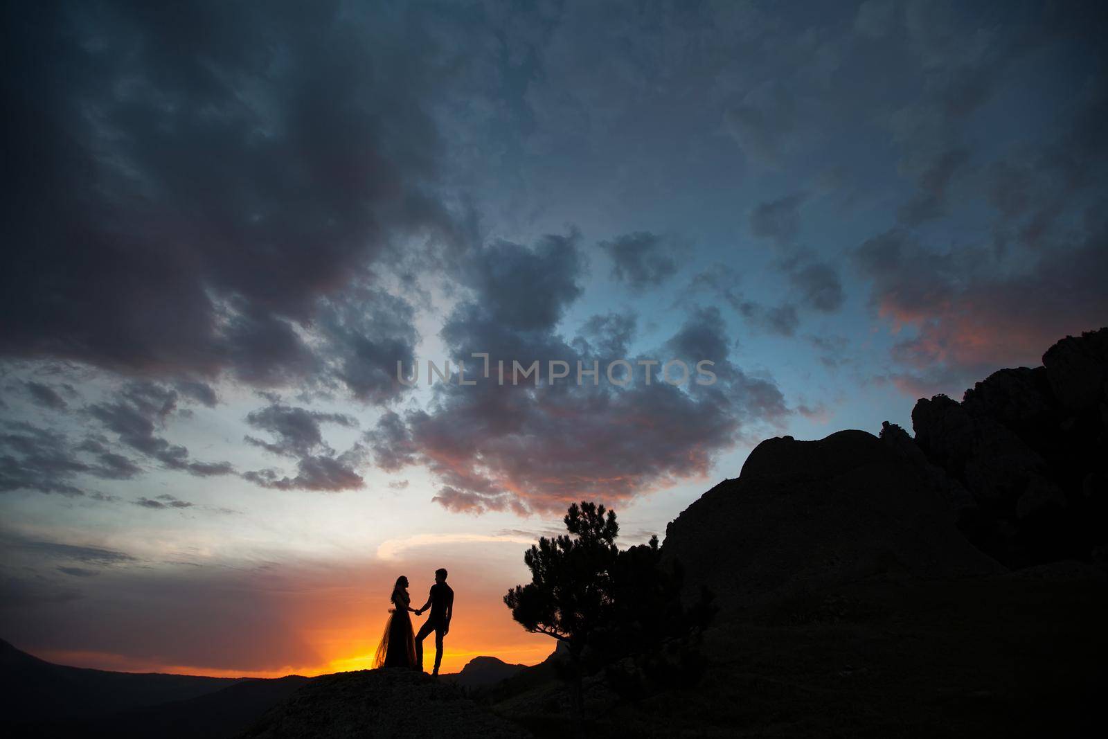 Silhouettes of a young couple lovers at sunset in rays of setting sun by StudioPeace