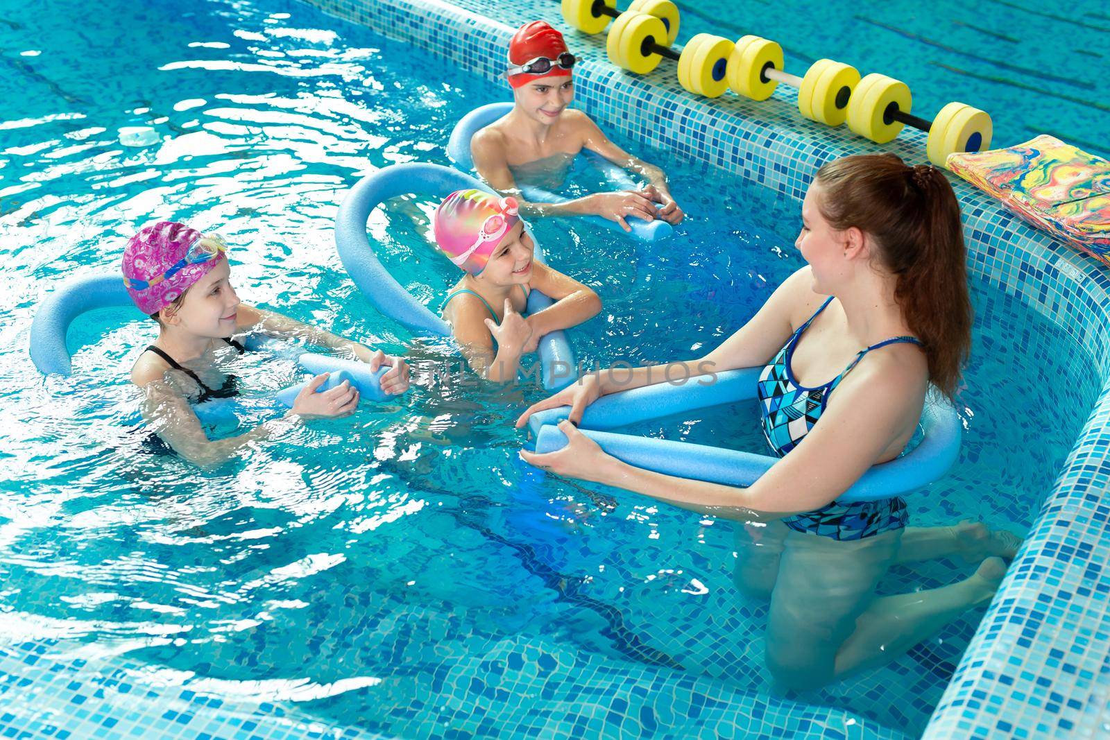 Young female instructor teaches children to swim in the pool by StudioPeace