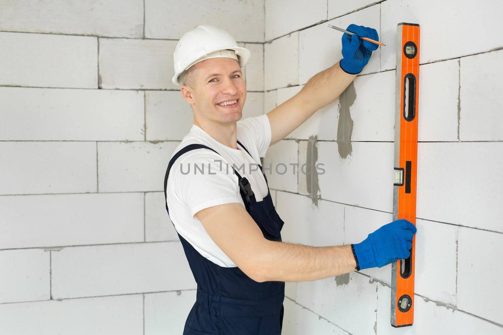 Beautiful young architect or builder in a white hard hat checks the level of the wall with the level tool by StudioPeace