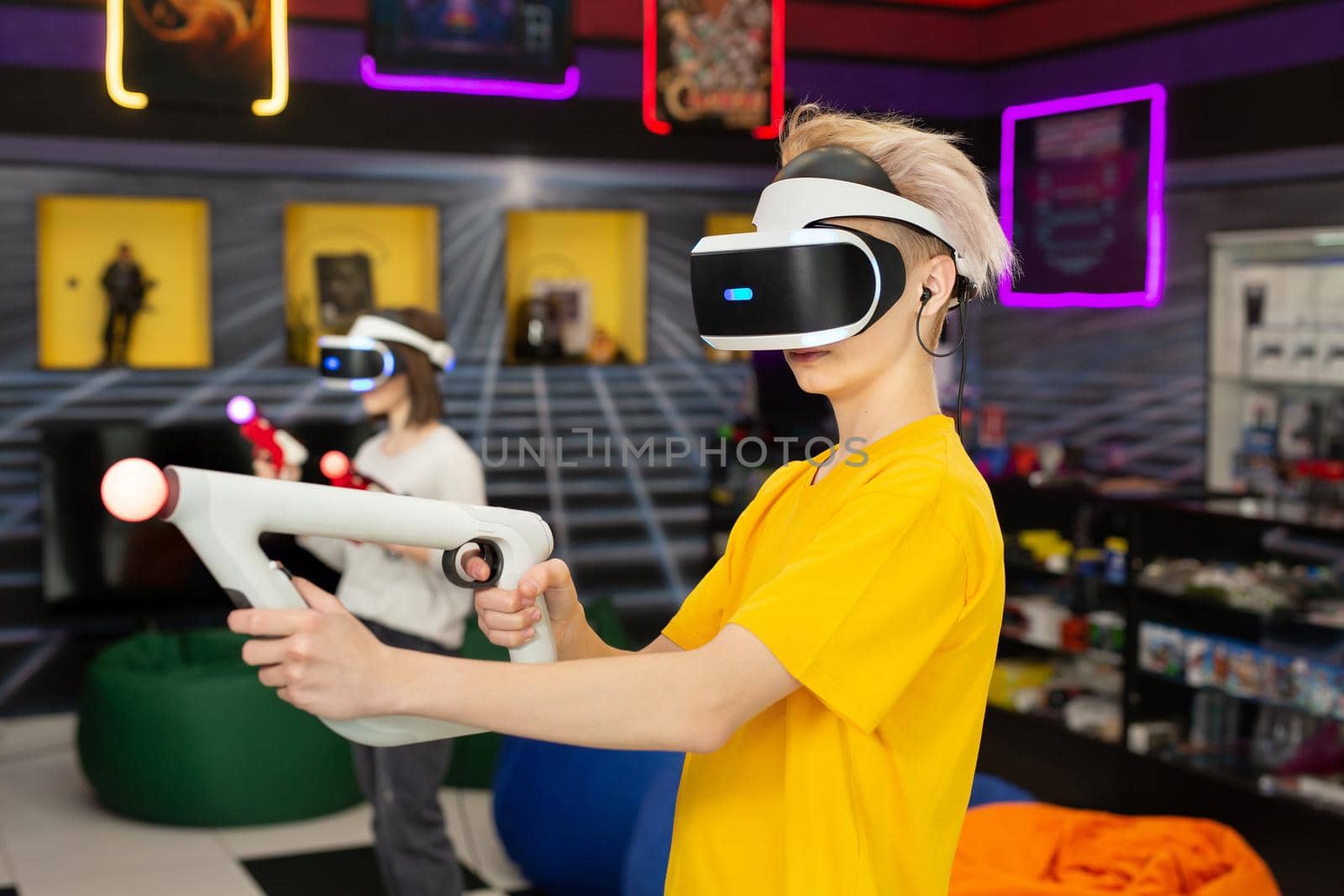 Teenage friends, a boy and a girl, with a virtual reality headset in glasses and hand motion controllers in the game club by StudioPeace