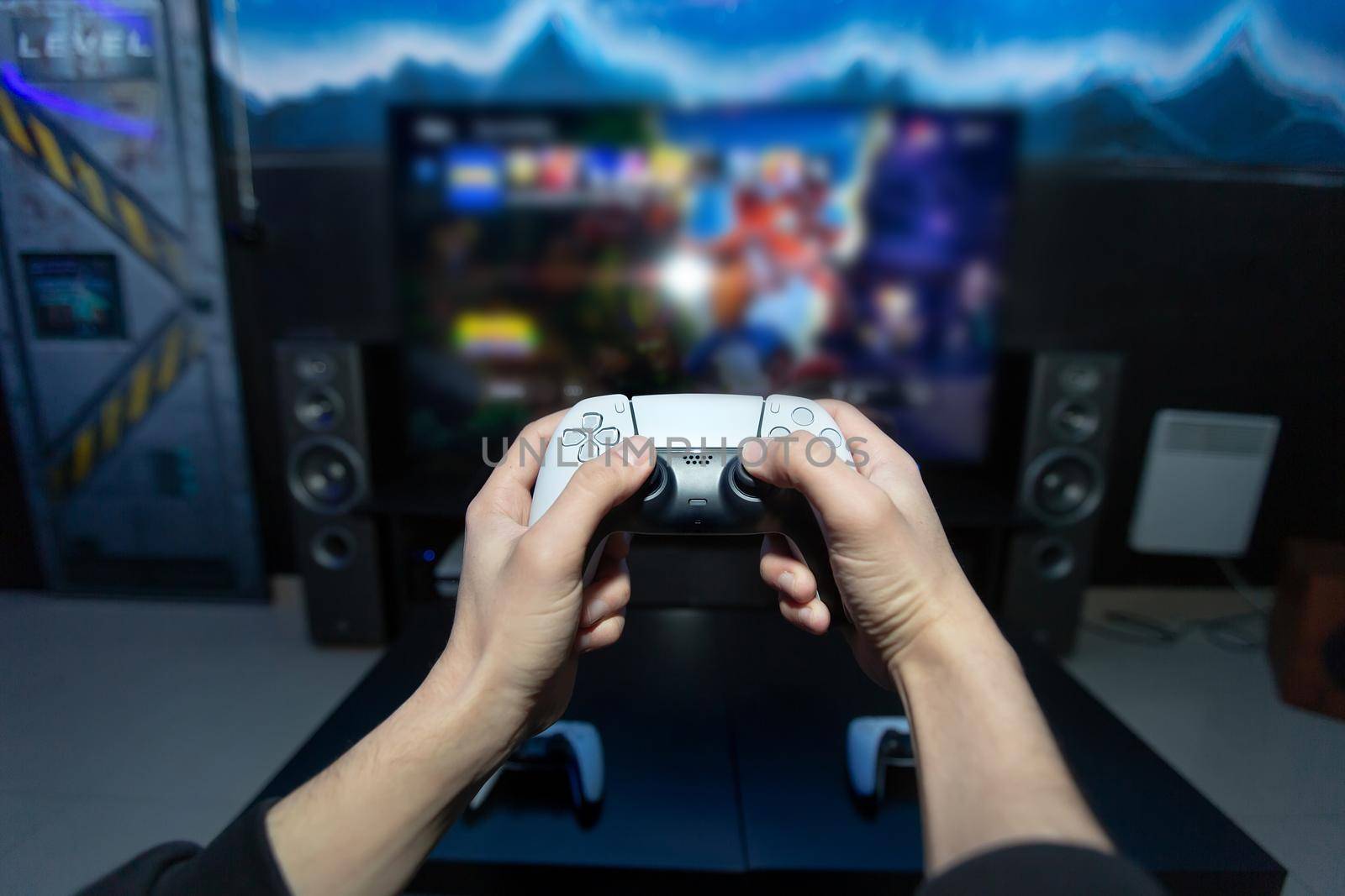 Close up of man hands holding wireless joysticks on foreground. Modern TV set with console.