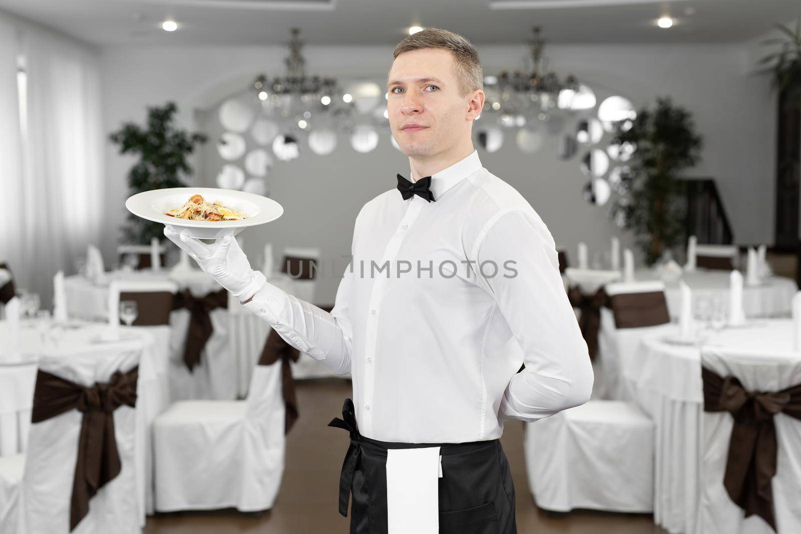 Young happy waiter while serving food in a restaurant by StudioPeace