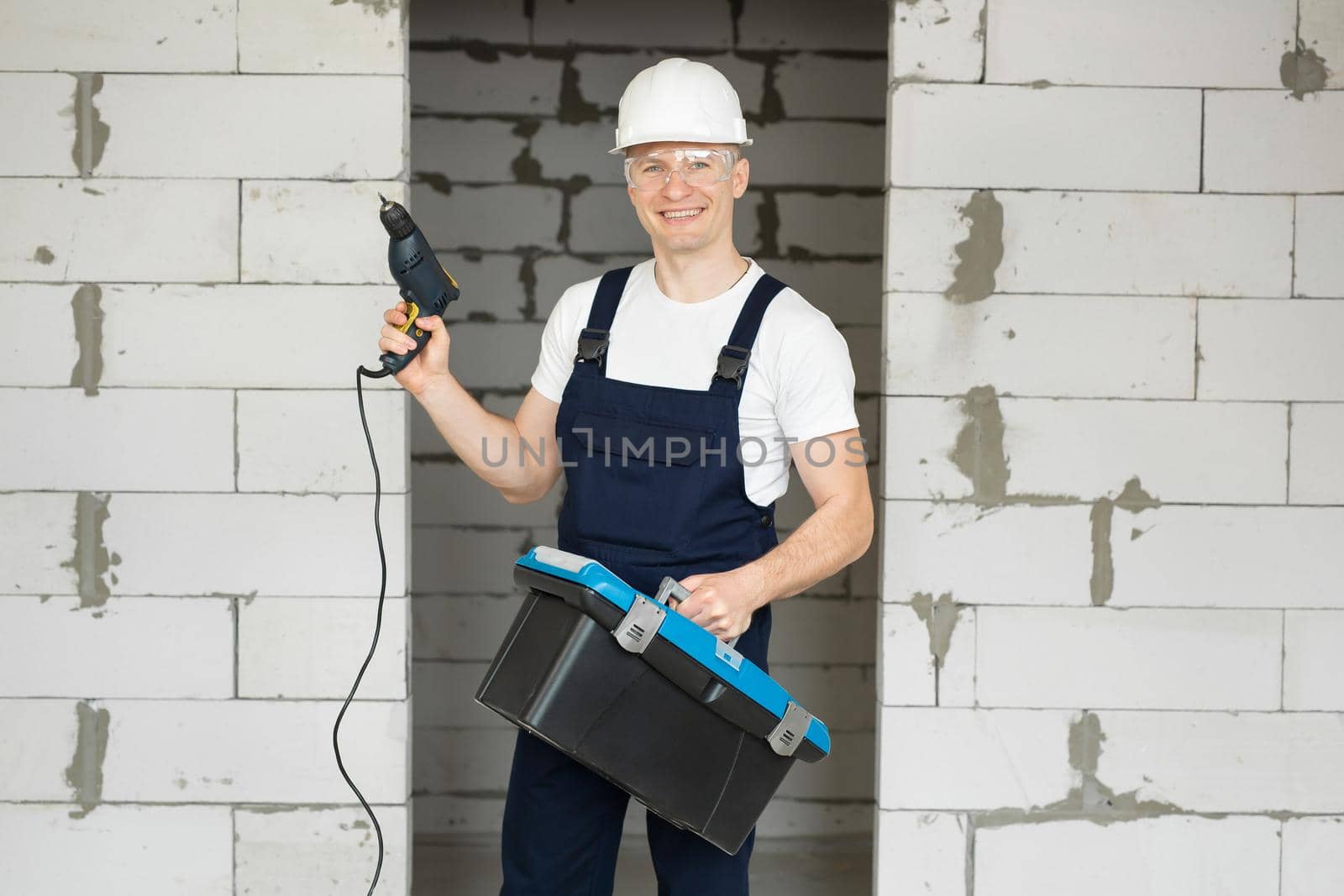 Male repairman in uniform and helmet holds a screwdriver and a toolbox.