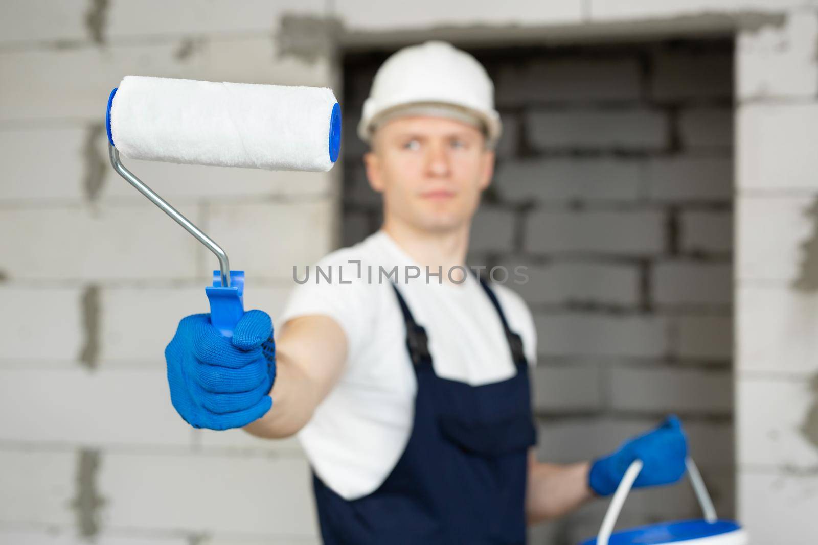 Male construction worker with a roller and paint on a construction site by StudioPeace