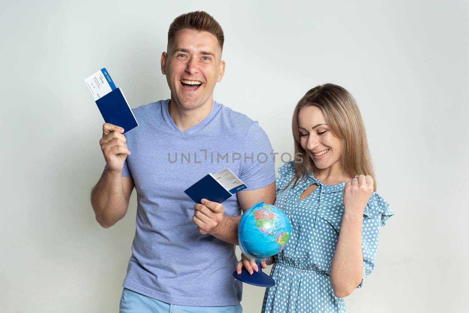 Cheerful young tourists in sunglasses, a guy and a girl isolated on a white background with a globe, passports and tickets in their hands by StudioPeace