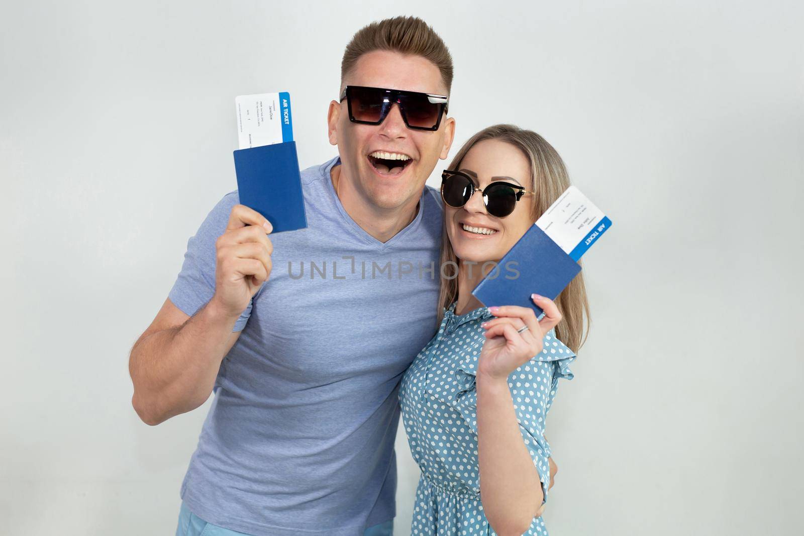 Cheerful young tourists in sunglasses, a guy and a girl isolated on a white background with passports and tickets in their hands by StudioPeace