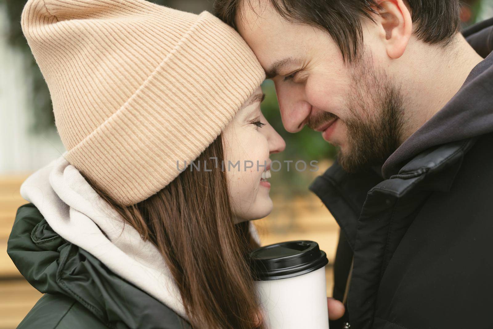 Loving beautiful couple on a winter day. A man hugging his happy woman, drinking hot tea or coffee while walking in the fresh air by StudioPeace