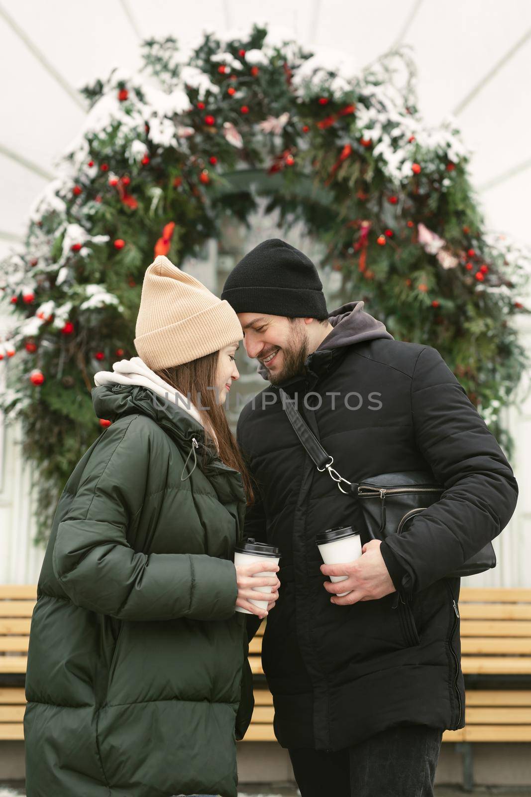 Loving beautiful couple on a winter day. A man hugging his happy woman, drinking hot tea or coffee while walking in the fresh air by StudioPeace