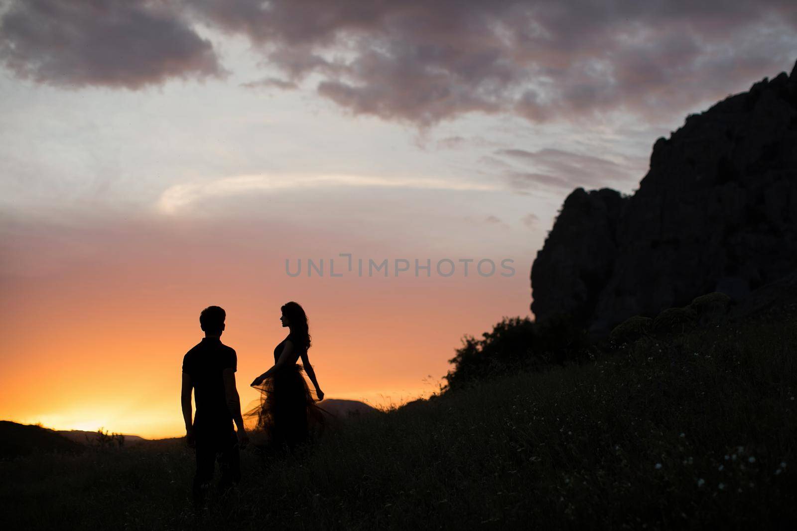 Silhouettes of a young couple lovers at sunset in rays of setting sun by StudioPeace