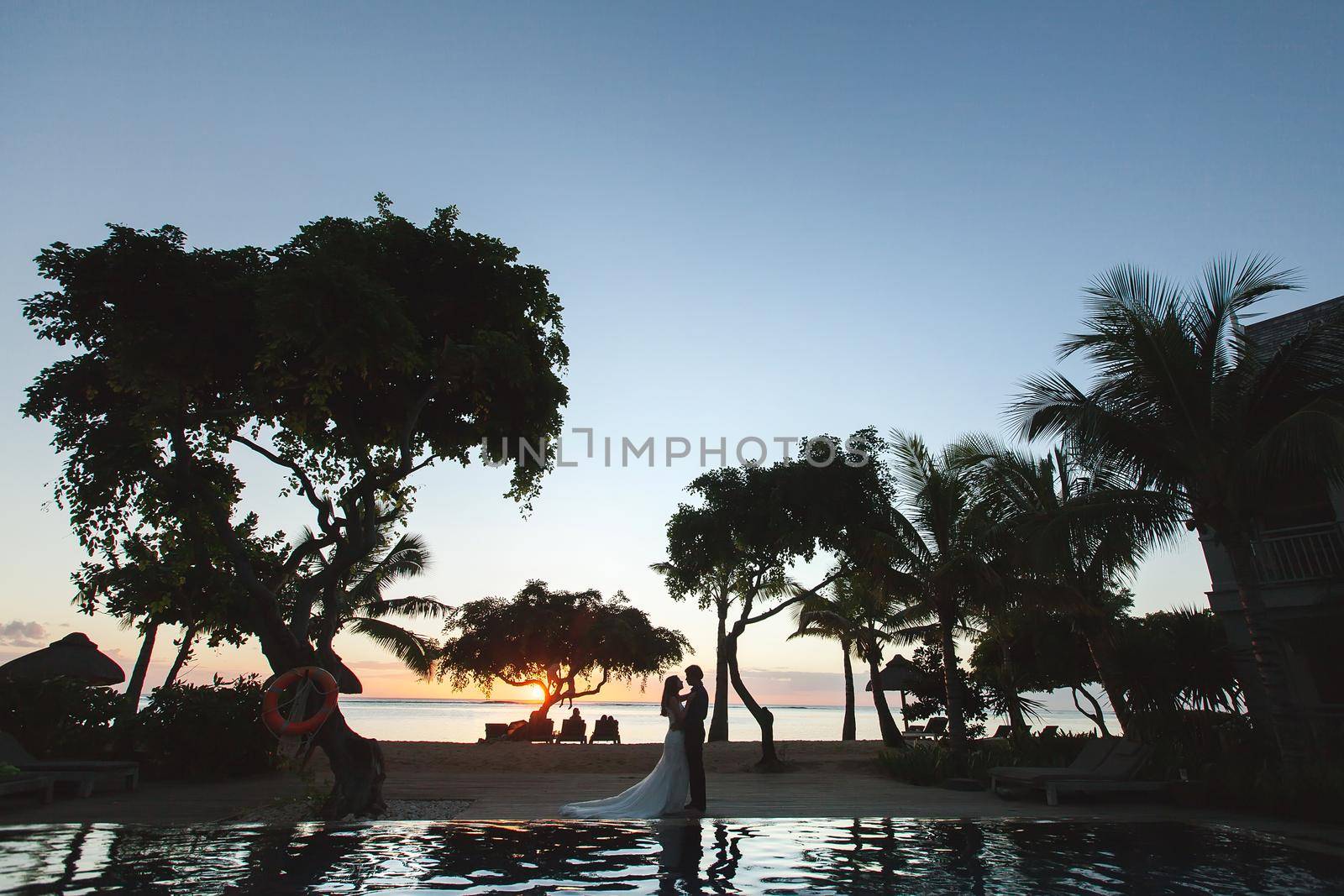 Silhouettes of the bride and groom at sunset. The reflection in the pool. by StudioPeace
