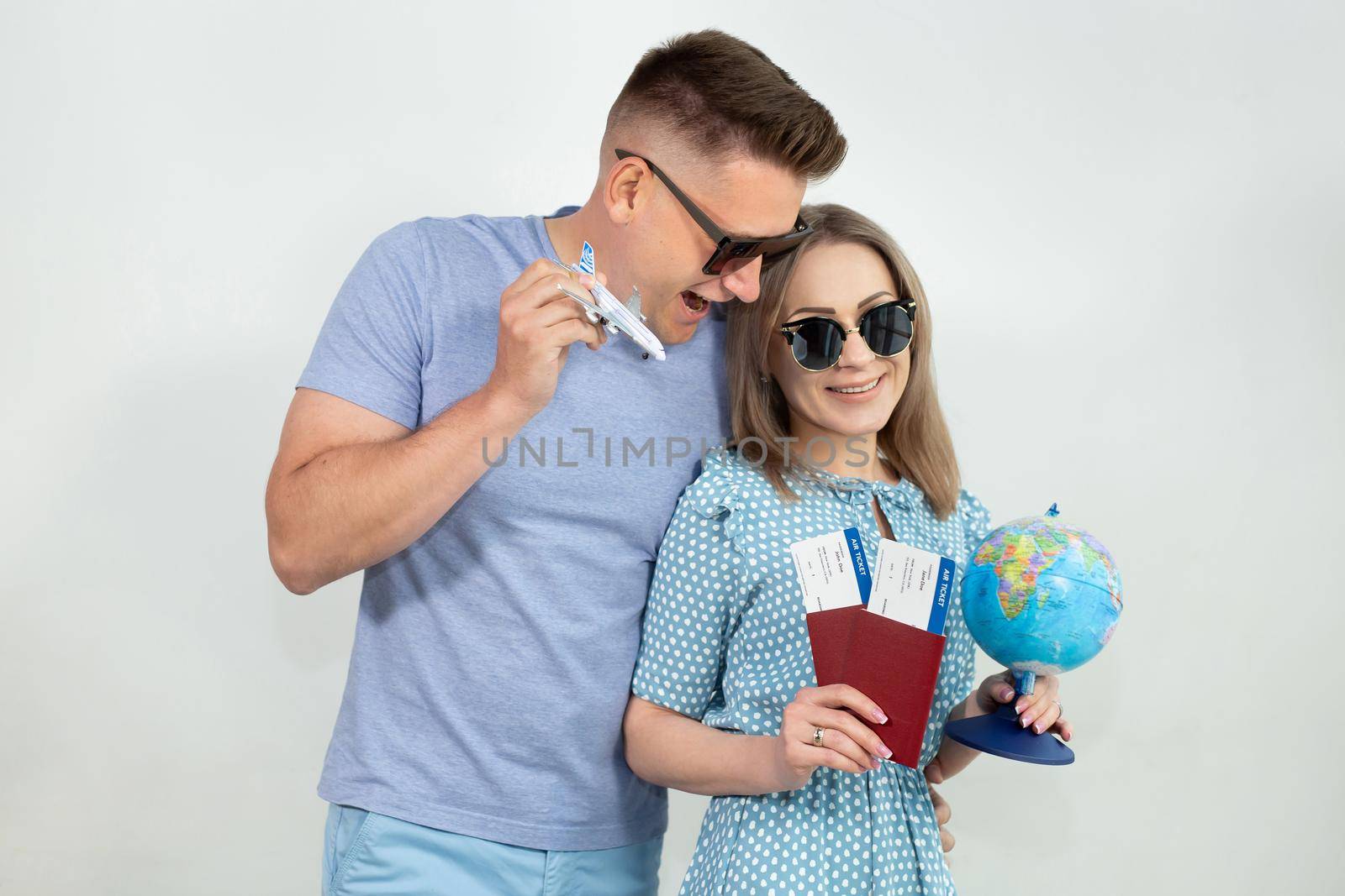 Excited young tourists in sunglasses, a guy and a girl isolated on a white background with a globe, passports, tickets and a model airplane in their hands.