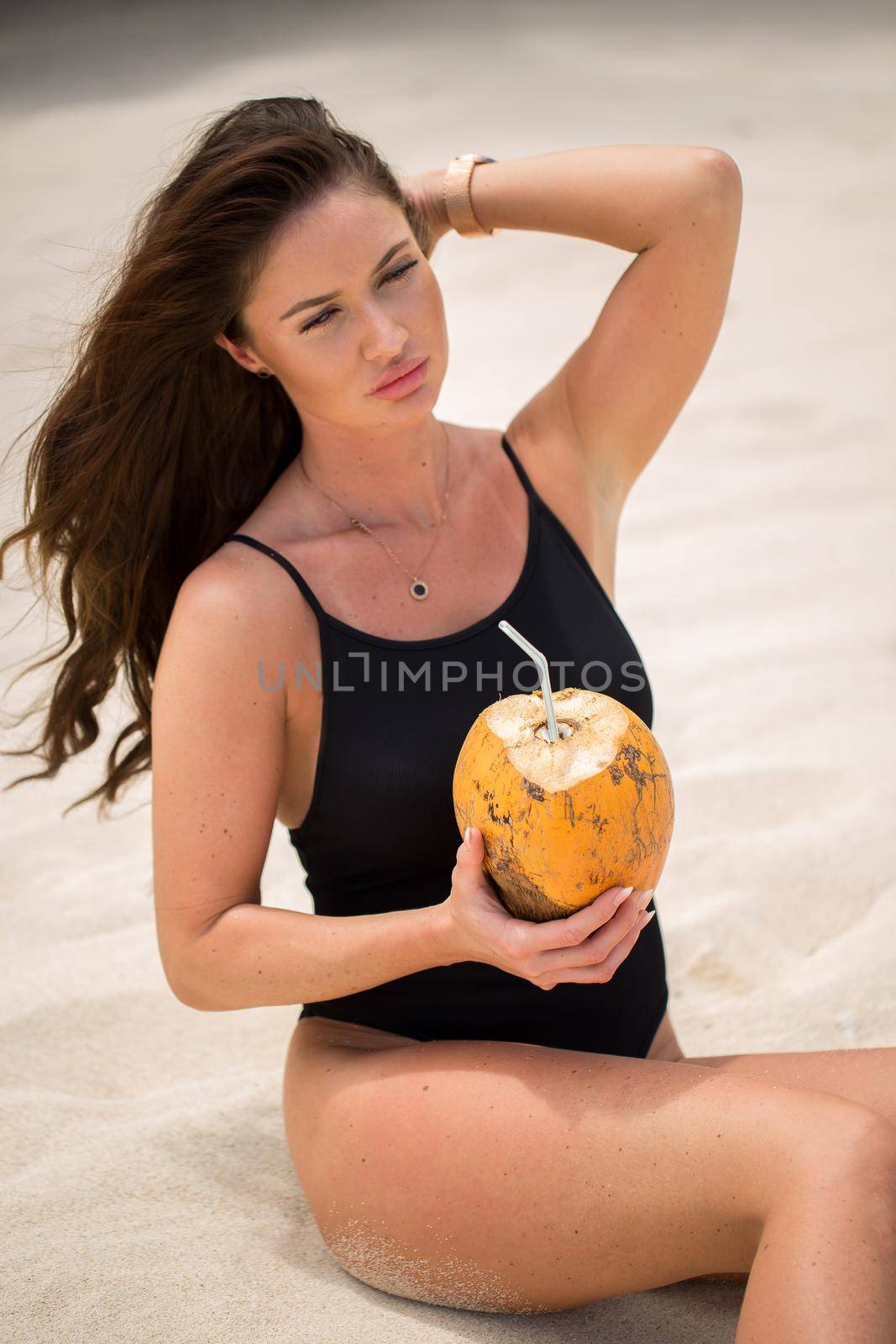 Young woman in black swimsuit with coconut cocktail on the beach