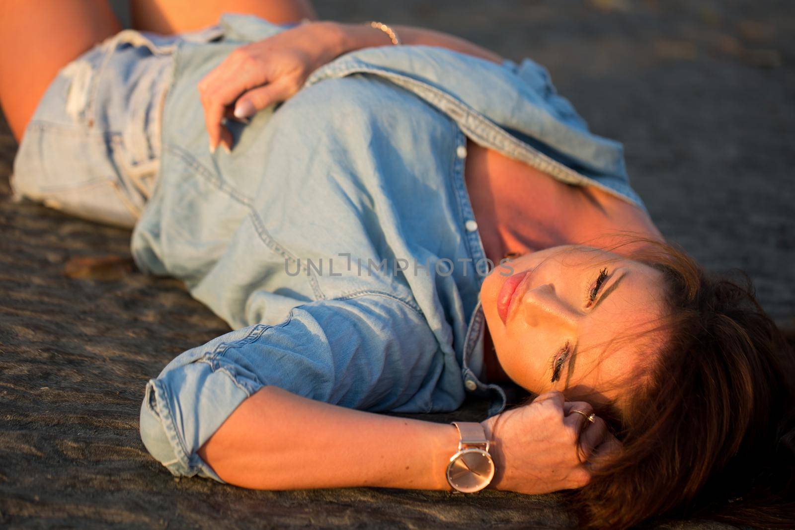 Young girl lying on the sand at sunset. by StudioPeace