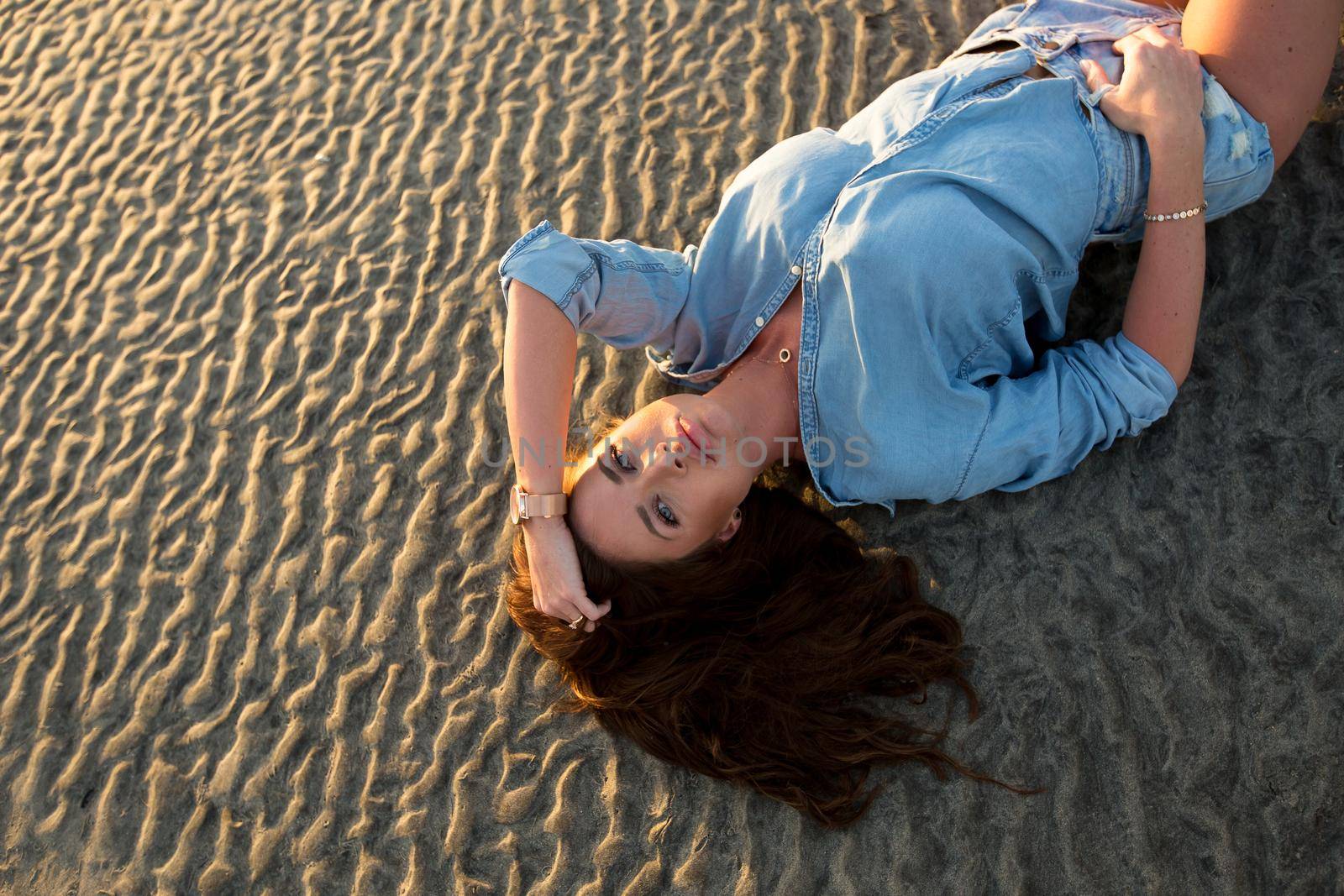 Young girl lying on the sand at sunset. by StudioPeace