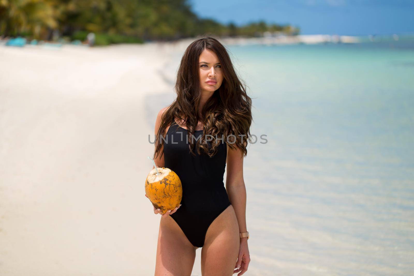 Young woman in black swimsuit with coconut cocktail on the beach