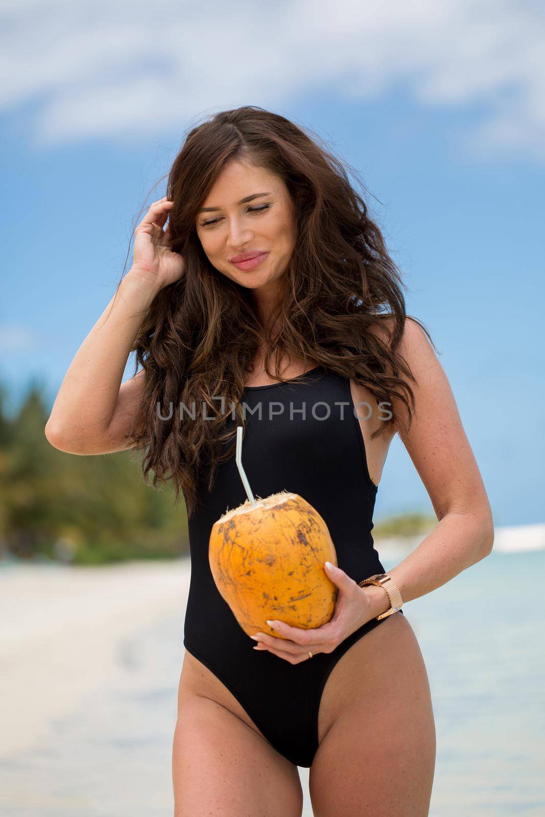 Young woman in black swimsuit with coconut cocktail on the beach. by StudioPeace
