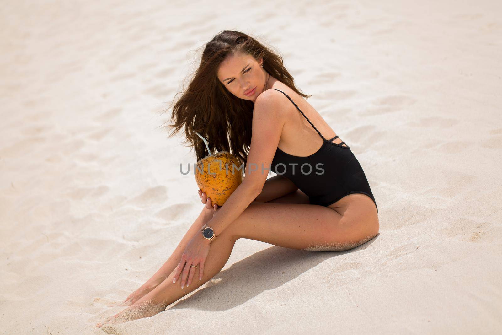 Young woman in black swimsuit with coconut cocktail on the beach