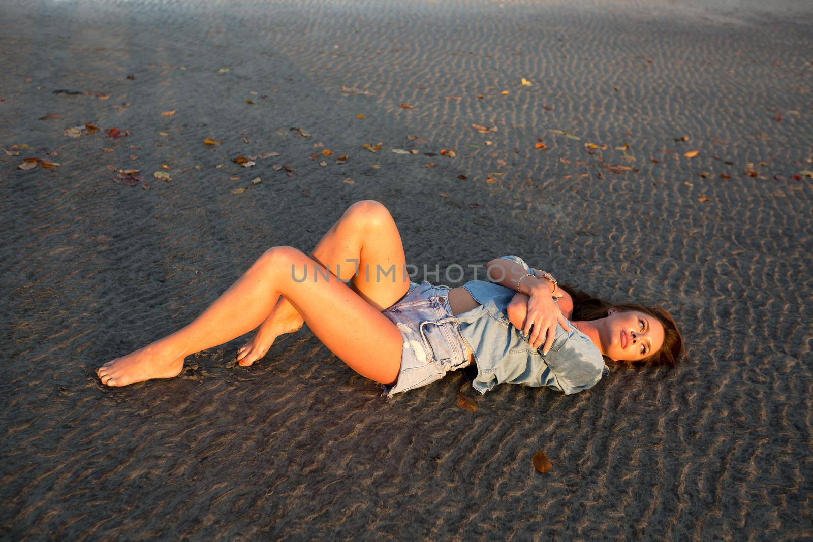 Young girl lying on the sand at sunset. by StudioPeace