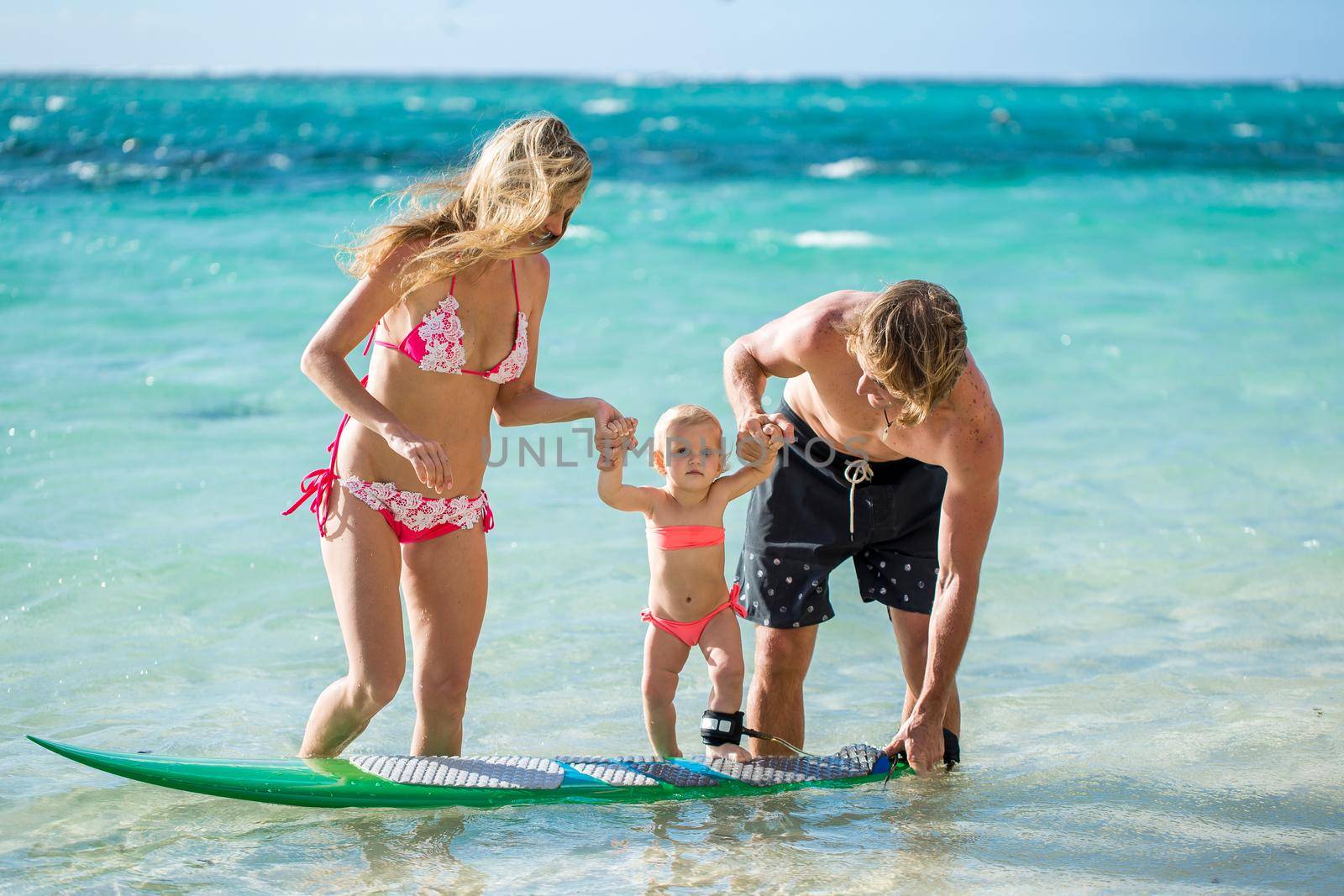 happy family teaching the daughter to stand on the surf in the ocean. concept about family, sport, active people. by StudioPeace