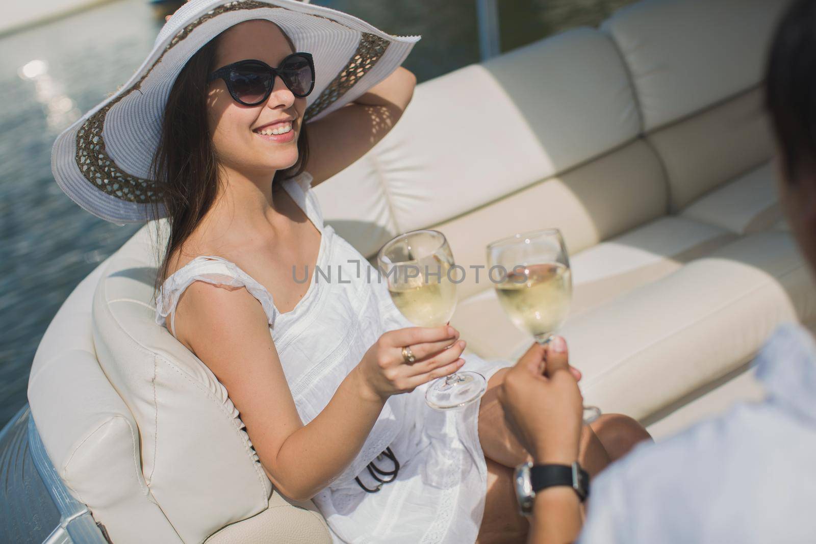 Smiling young couple holding glasses with champagne and looking at each other while sitting on the board of yacht. by StudioPeace