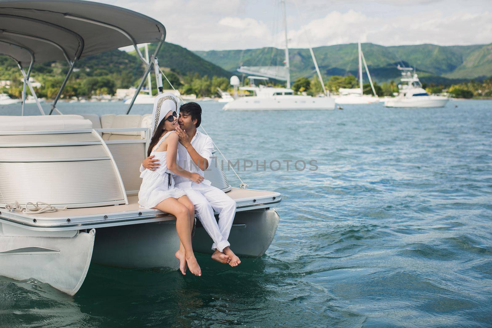 Young couple is traveling on a yacht in the Indian ocean. Man and a woman sit on the edge of the boat and kiss. by StudioPeace