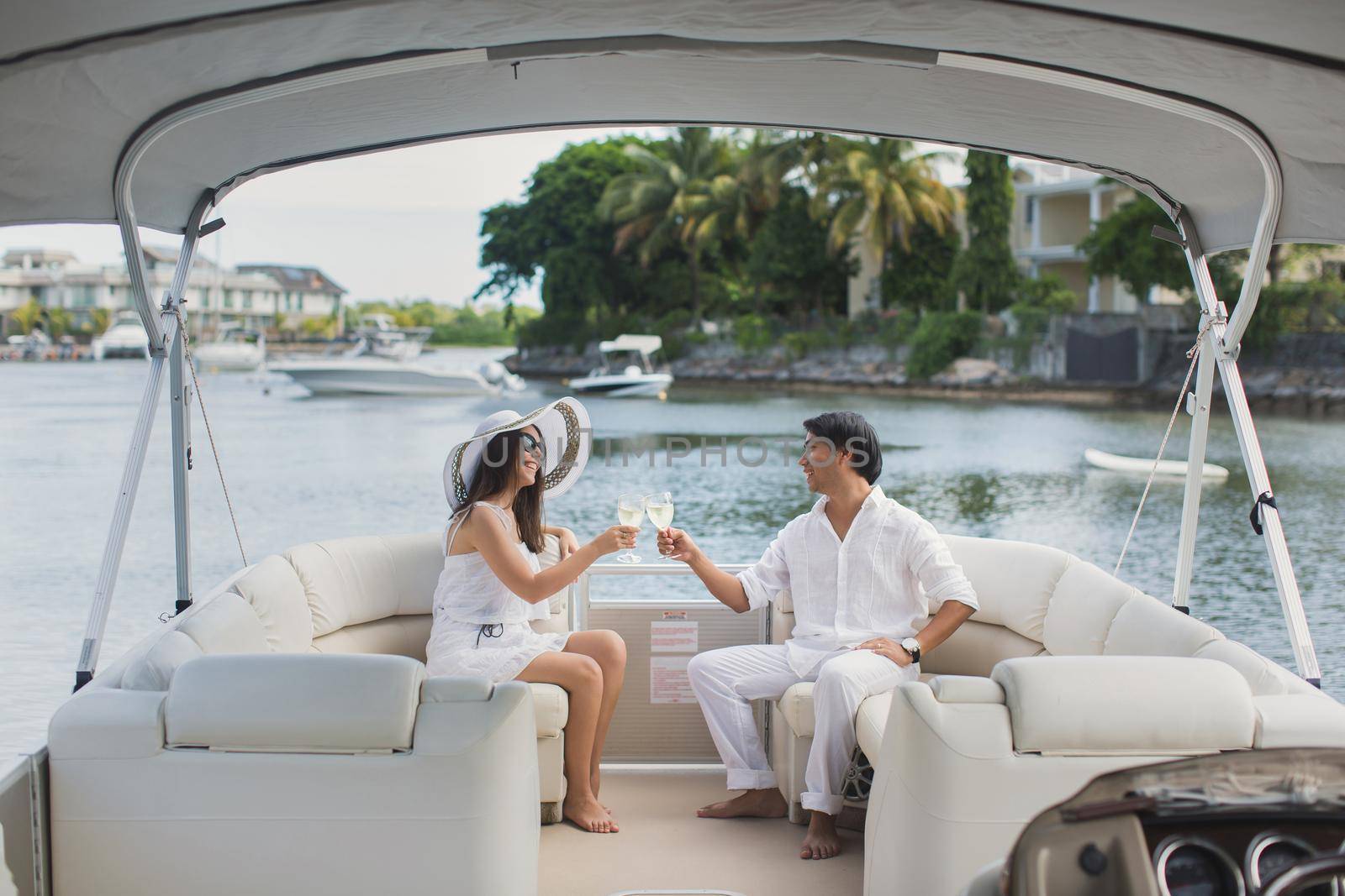 Smiling young couple holding glasses with champagne and looking at each other while sitting on the board of yacht