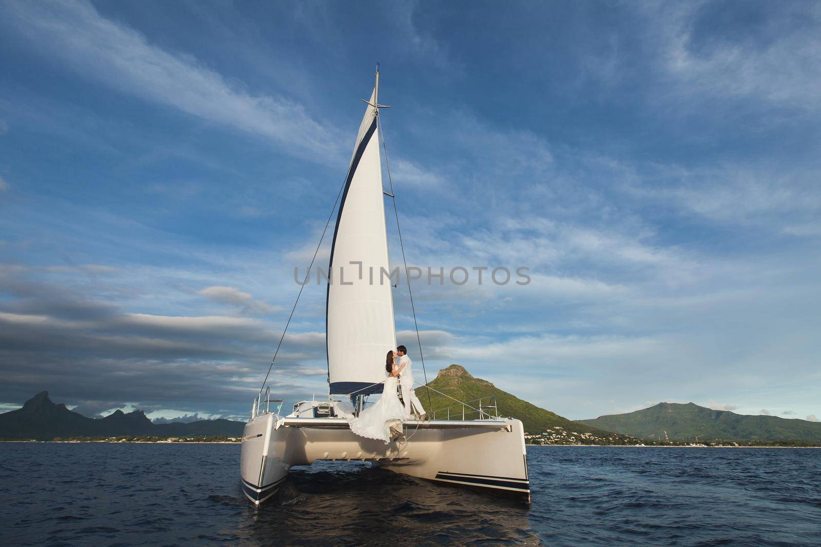 Beautiful wedding couple bride and groom on yacht at wedding day outdoors in the sea. Happy marriage couple kissing on boat in ocean. Stylish Marine wedding.
